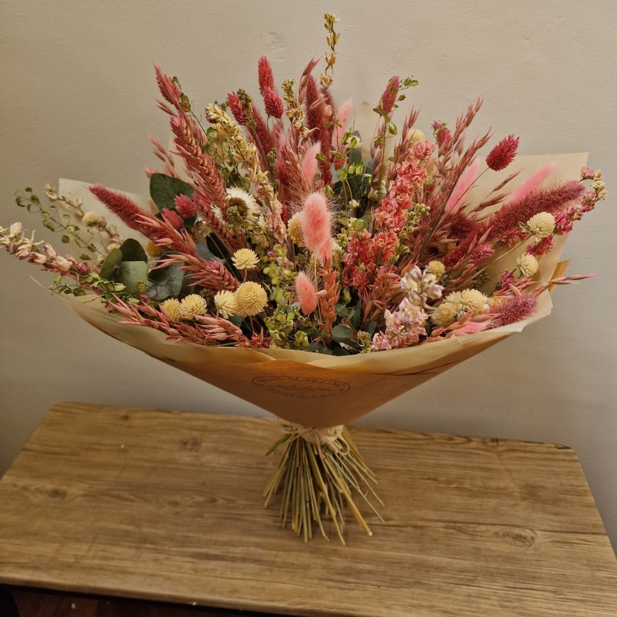 Luxury hand-tied dried flower bouquet featuring preserved pink flowers, natural grasses and textured foliage in soft blush and neutral tones.