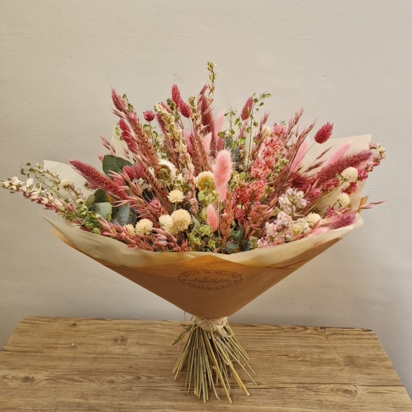 Luxury hand-tied dried flower bouquet featuring preserved pink flowers, natural grasses and textured foliage in soft blush and neutral tones.