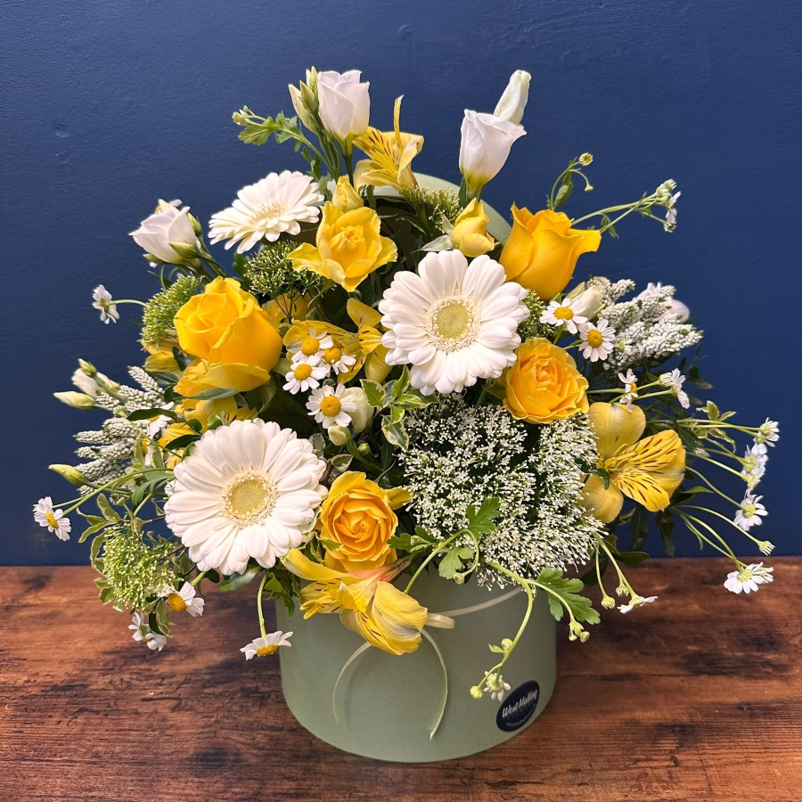 Yellow and white spring flowers arranged in a pale green hat box