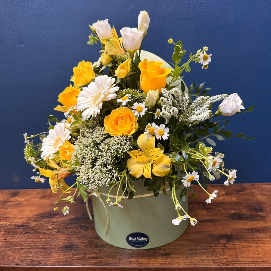 Yellow and white spring flowers arranged in a pale green hat box