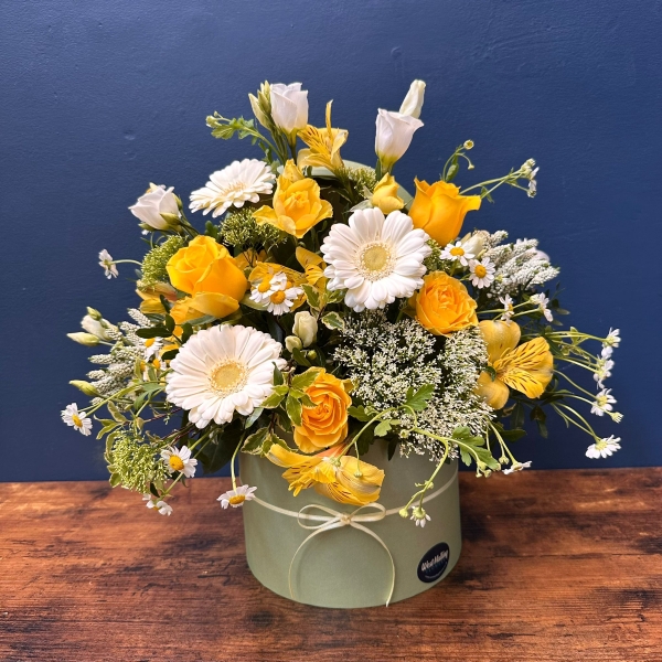 Yellow and white spring flowers arranged in a pale green hat box