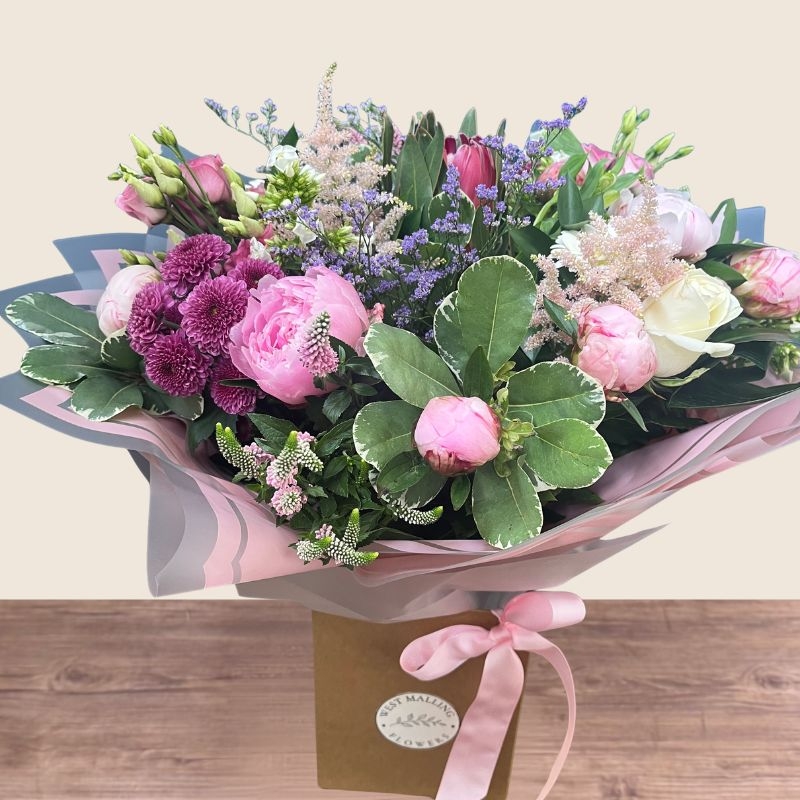 Luxury hand-tied bouquet featuring pink peonies, white flowers and lilac seasonal flowers arranged in a romantic garden style.