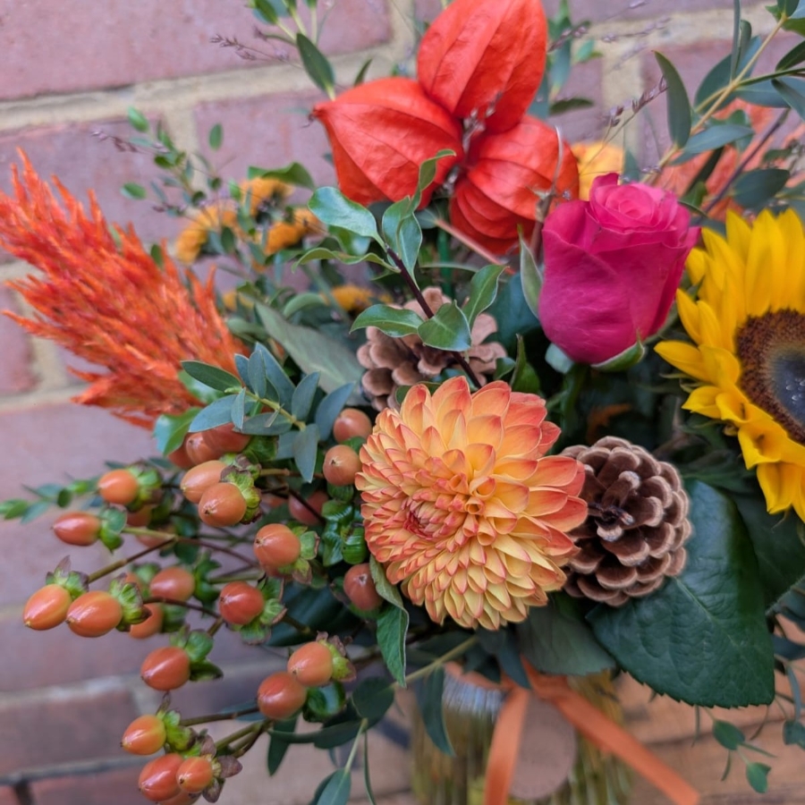 Autumn Glow yellow glass vase arrangement with orange, raspberry, bronze and golden seasonal flowers