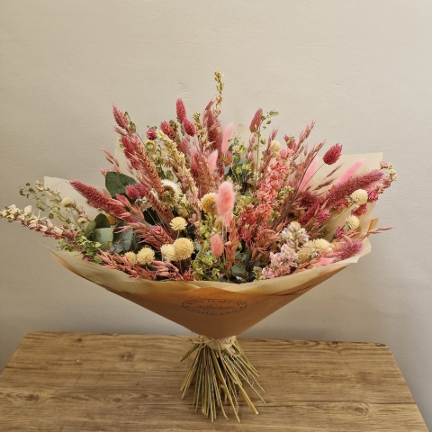 Luxury hand-tied dried flower bouquet featuring preserved pink flowers, natural grasses and textured foliage in soft blush and neutral tones.