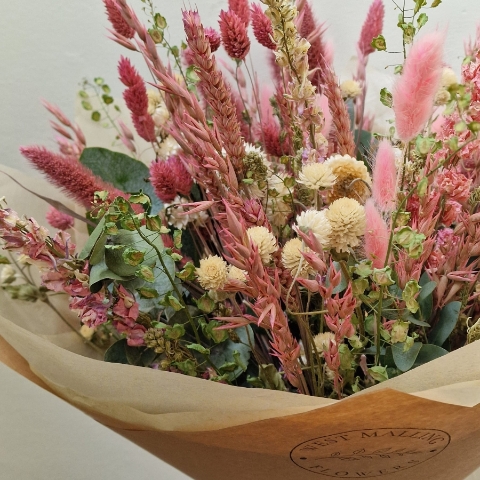 Luxury hand-tied dried flower bouquet featuring preserved pink flowers, natural grasses and textured foliage in soft blush and neutral tones.