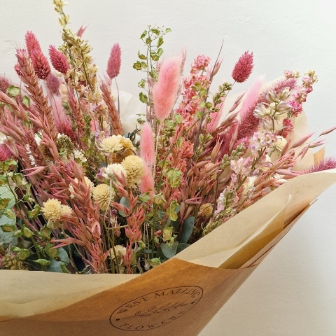 Luxury hand-tied dried flower bouquet featuring preserved pink flowers, natural grasses and textured foliage in soft blush and neutral tones.