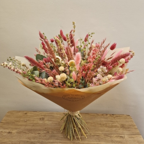 Luxury hand-tied dried flower bouquet featuring preserved pink flowers, natural grasses and textured foliage in soft blush and neutral tones.