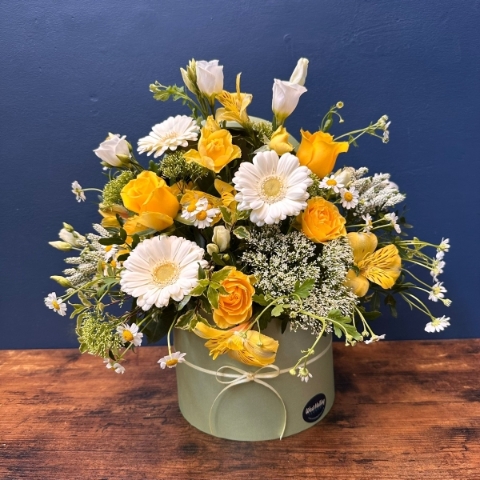 Yellow and white spring flowers arranged in a pale green hat box