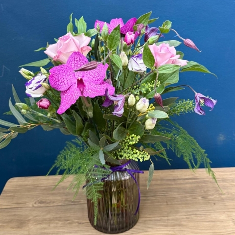 Vibrant summer flower arrangement in coloured glass vase with pink purple orange and cerise flowers