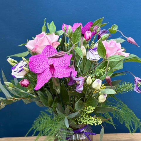 Vibrant summer flower arrangement in coloured glass vase with pink purple orange and cerise flowers