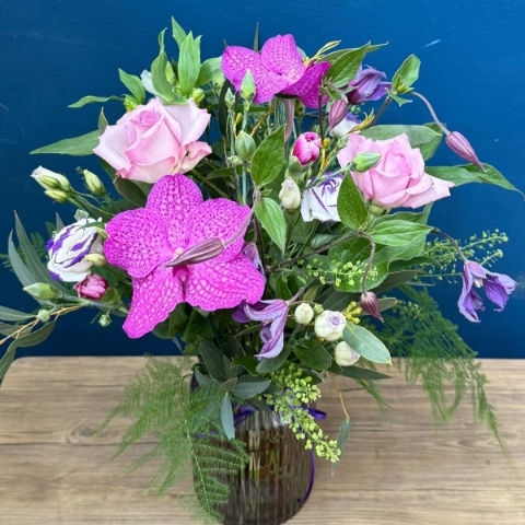 Vibrant summer flower arrangement in coloured glass vase with pink purple orange and cerise flowers