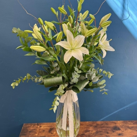 Tall white lily arrangement in glass vase with foliage and decorative twigs